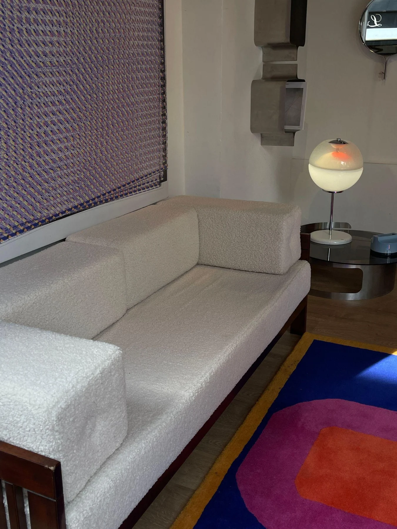 Patterned wall art above a white sofa beside a vivid geometric rug.
