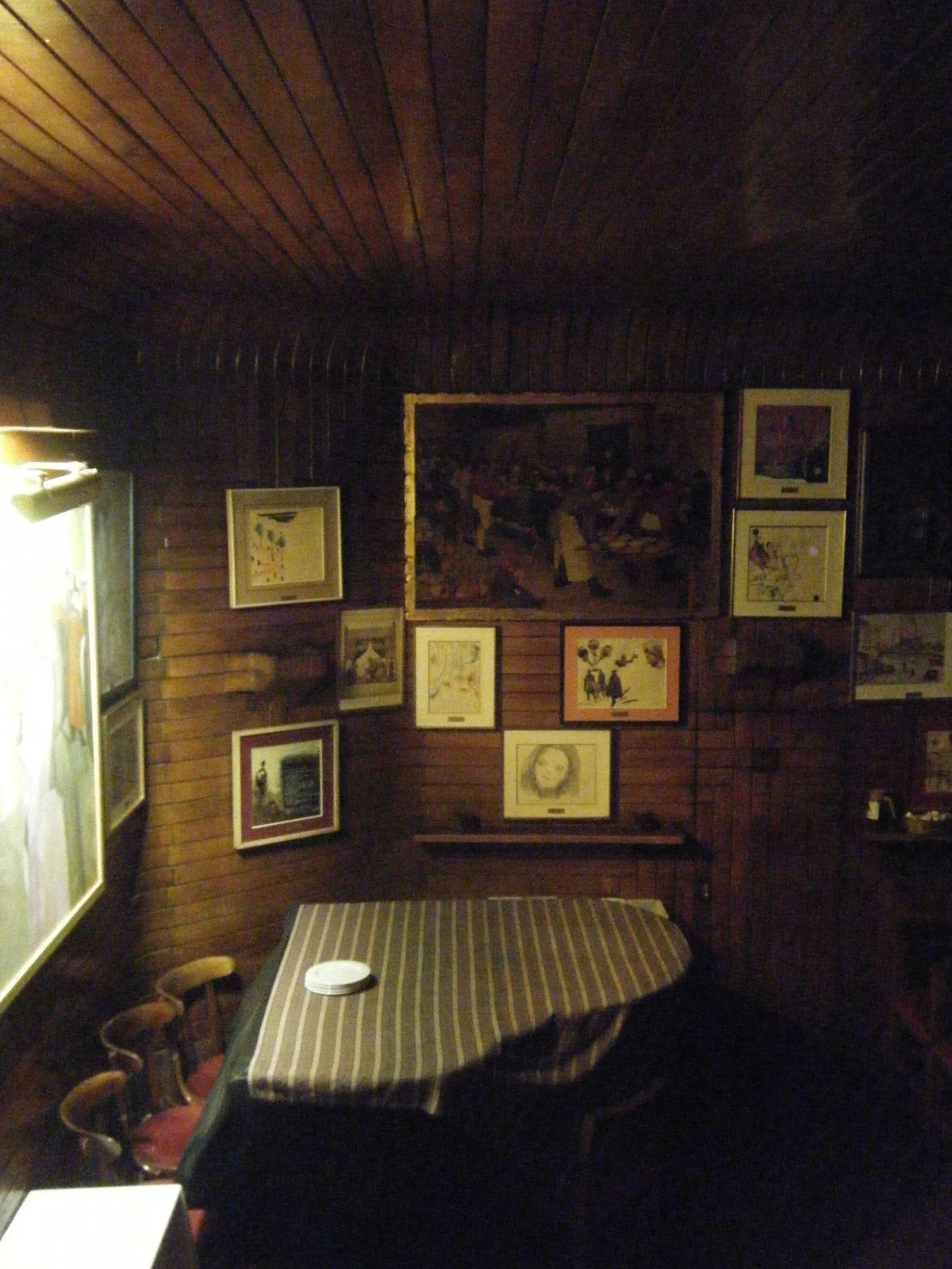 A group of framed artworks on dark timber walls above a table.