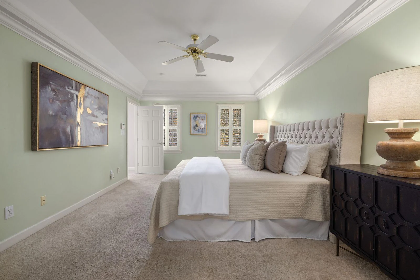 Soft neutral bedroom with a large muted painting on a pale green wall.