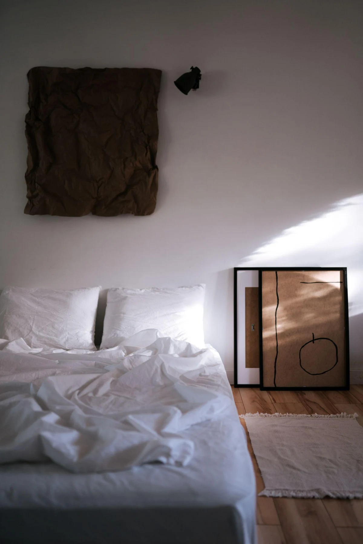 A dark textured artwork contrasts with pale walls and white bed linen.