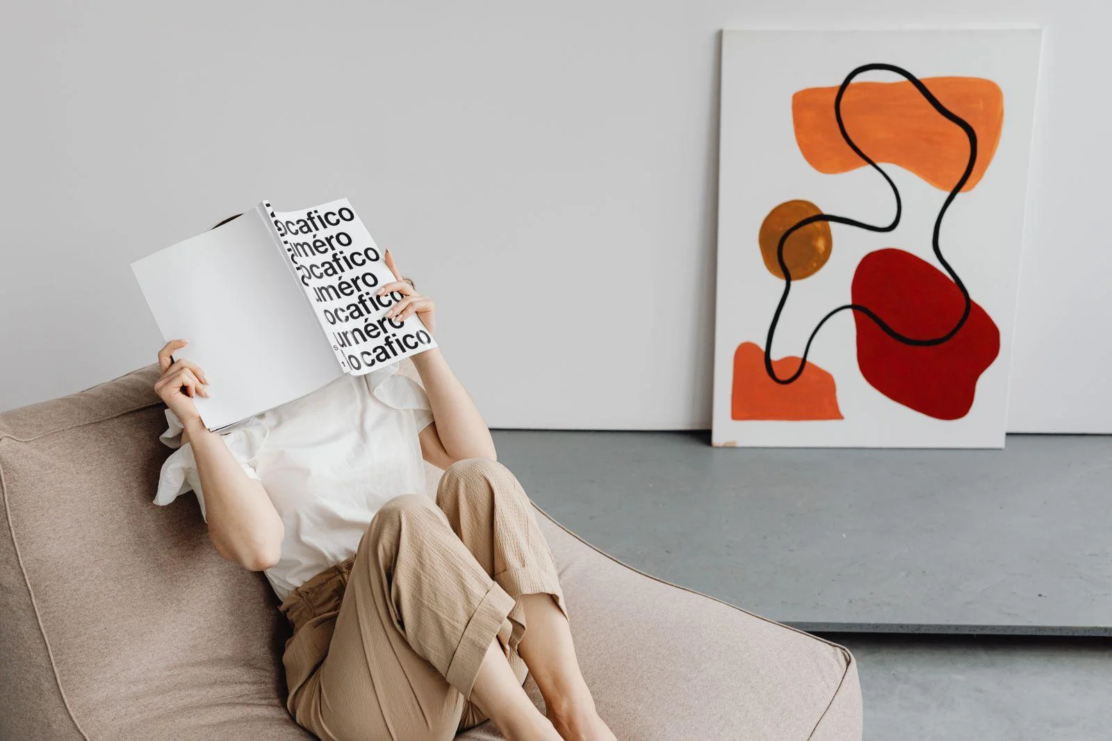 A person reading beside abstract artwork in a neutral sitting area.