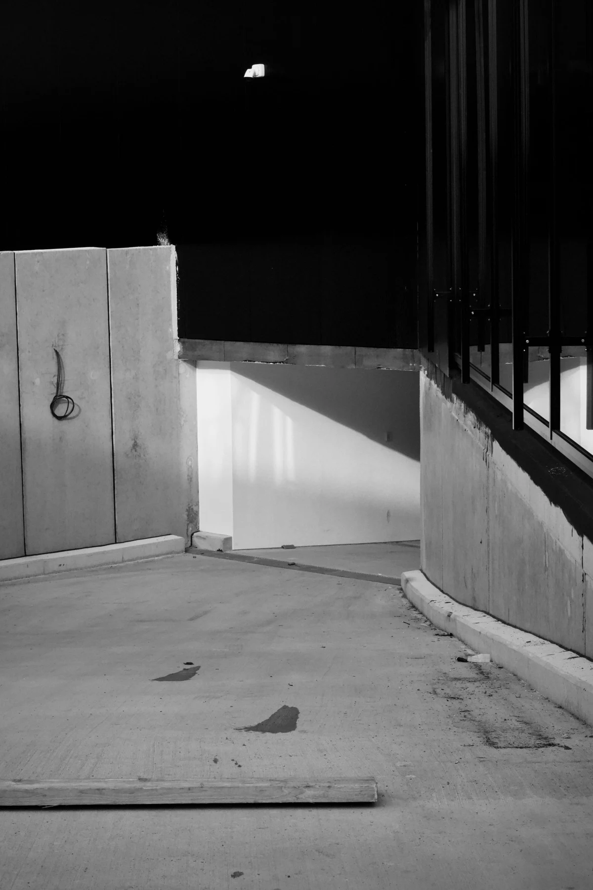 Black and white architectural photograph with a white concrete wall, dark opening, and strong diagonal shadow.