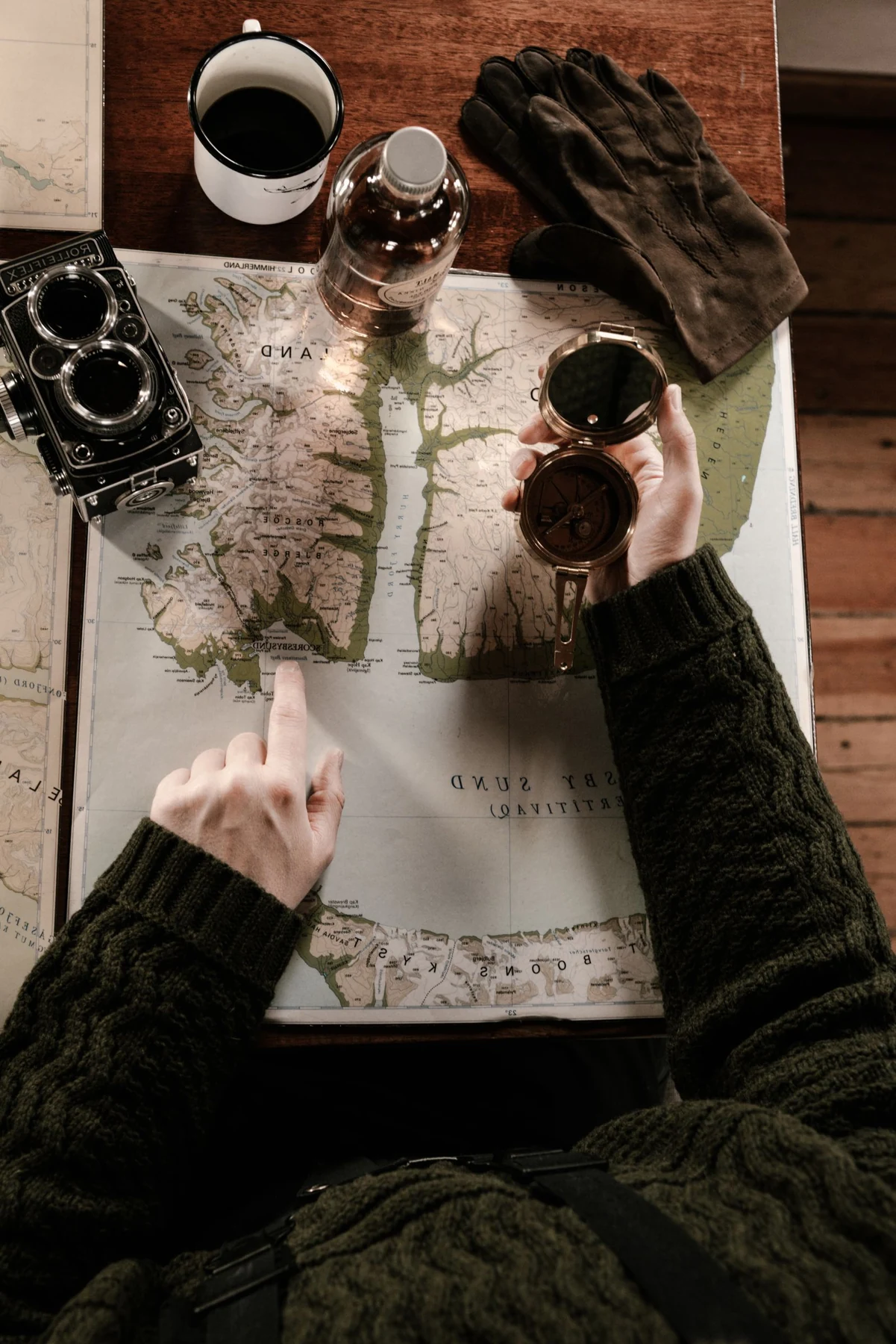A printed map spread on a table with a compass and camera, showing its detailed lines and muted colors.