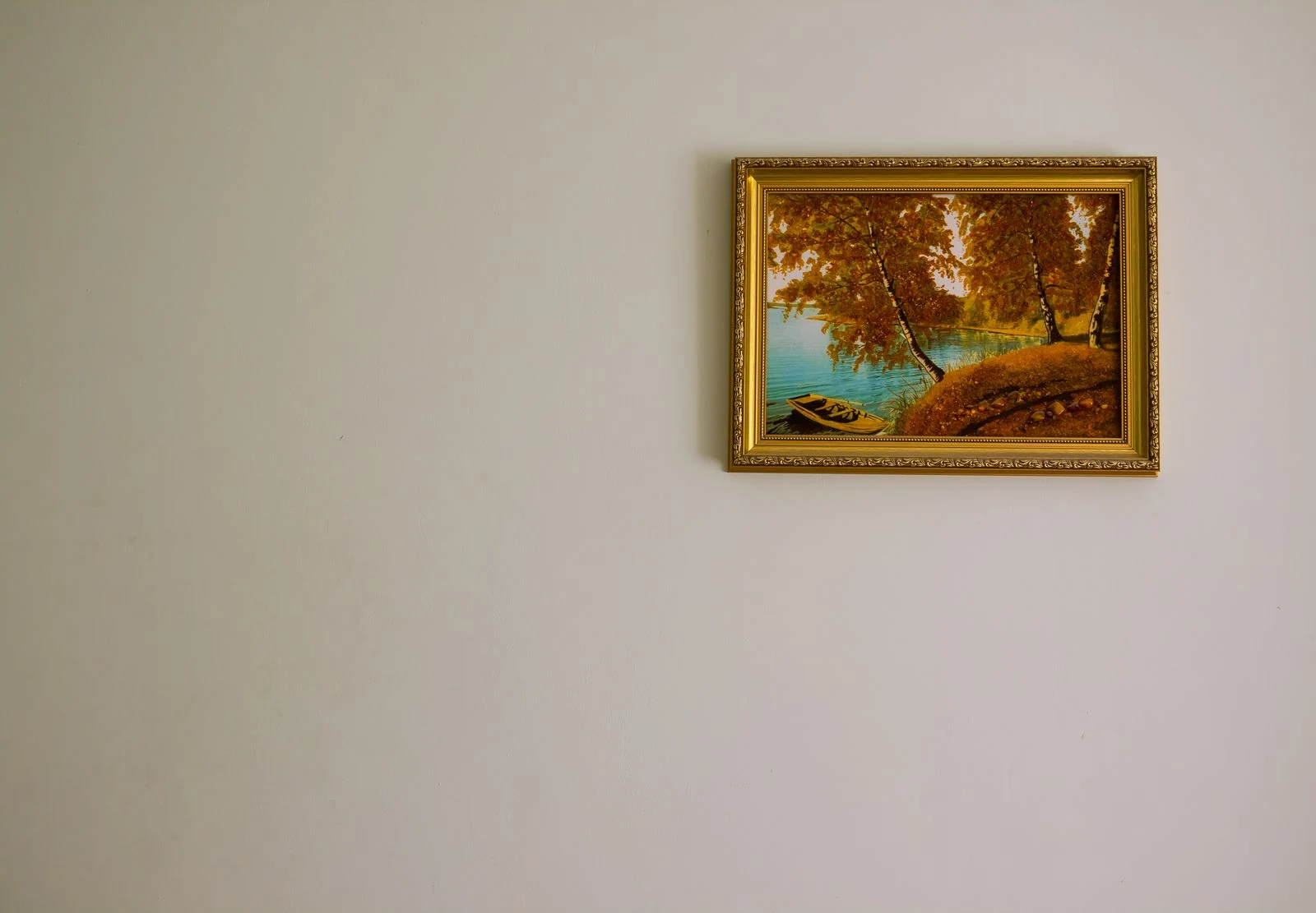 A traditional autumn landscape painting in a gold frame on a plain light wall.