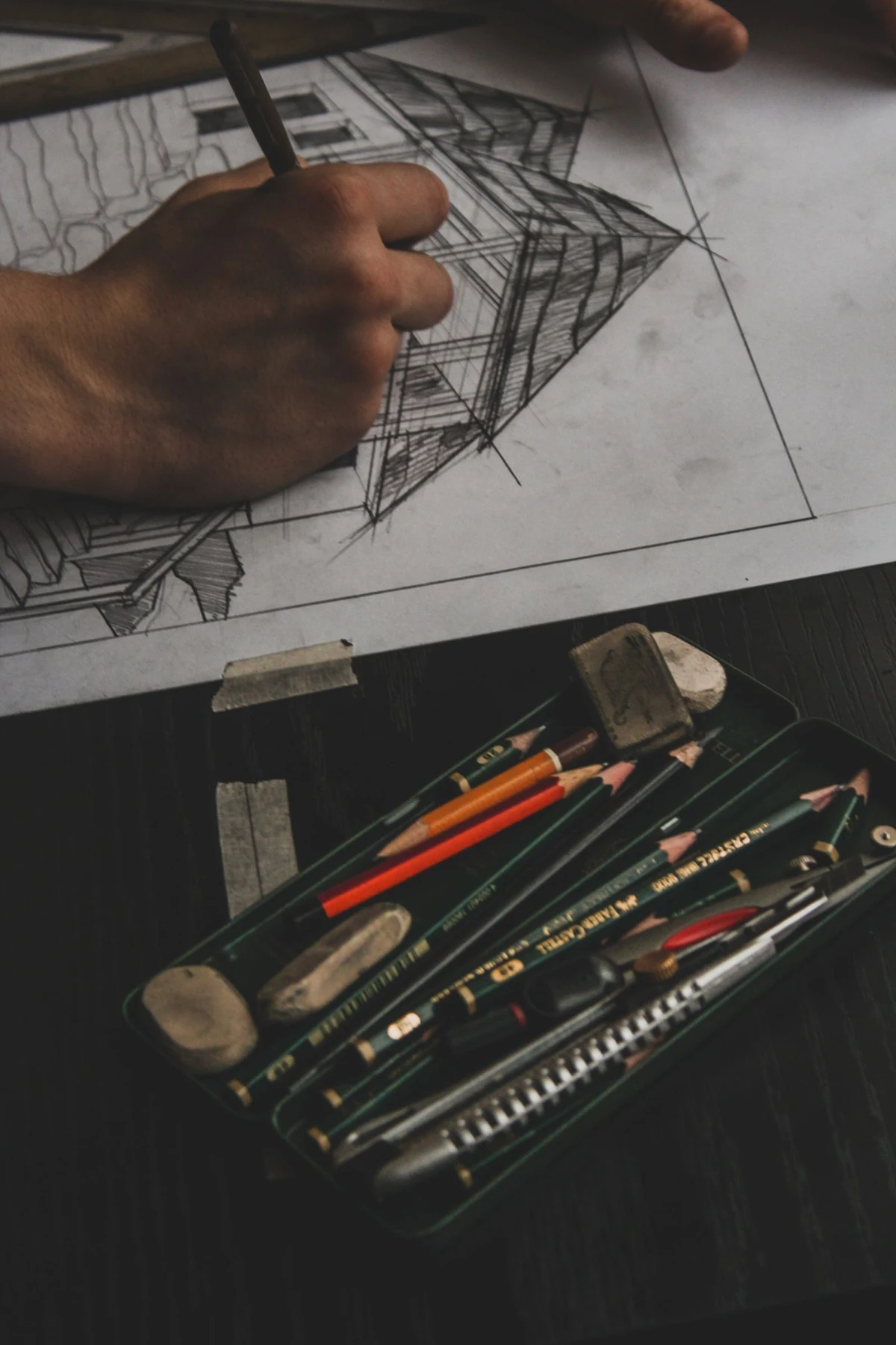 A hand works on a detailed perspective drawing of a building beside drawing tools.