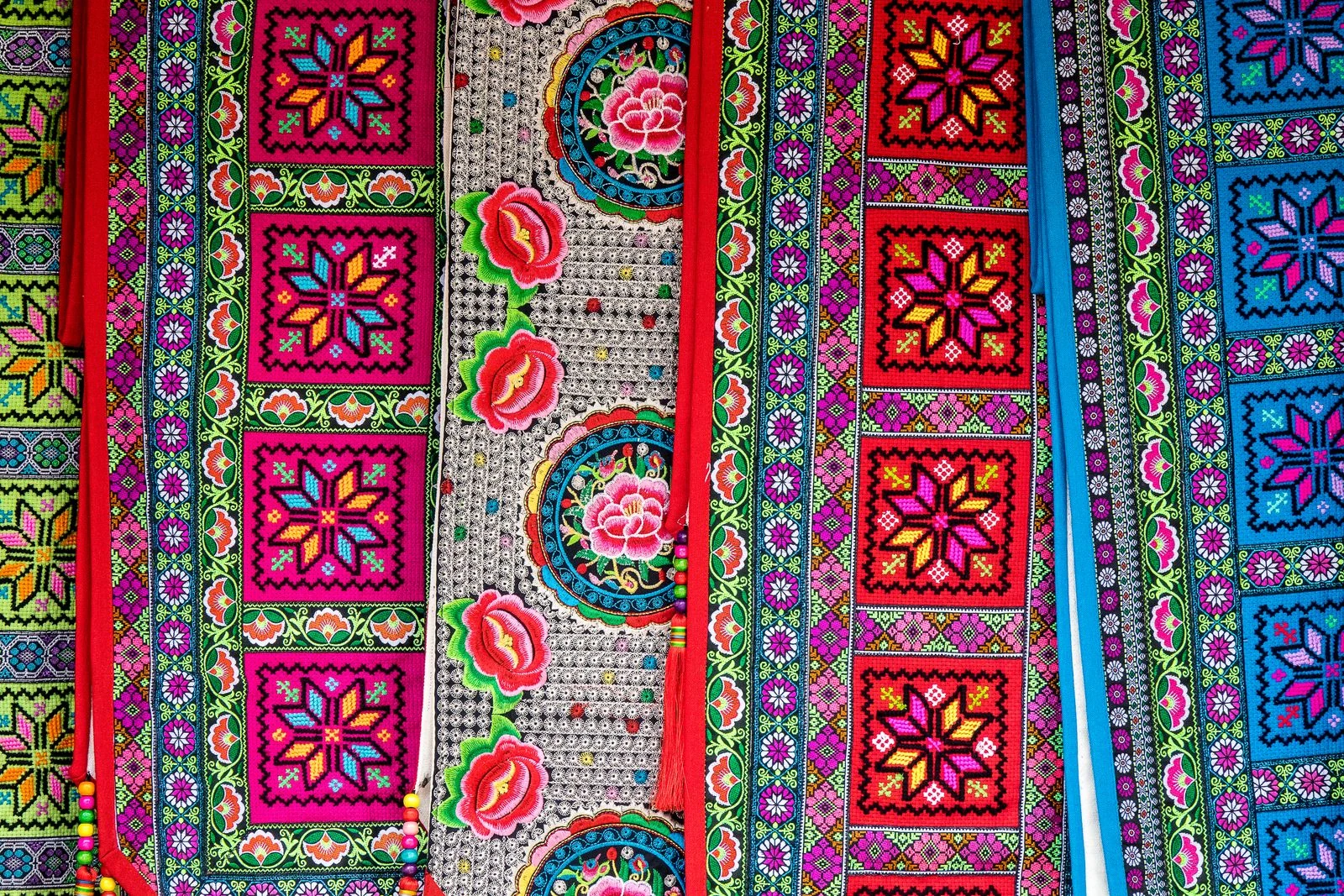 A close view of colorful embroidered geometric and floral textile patterns.