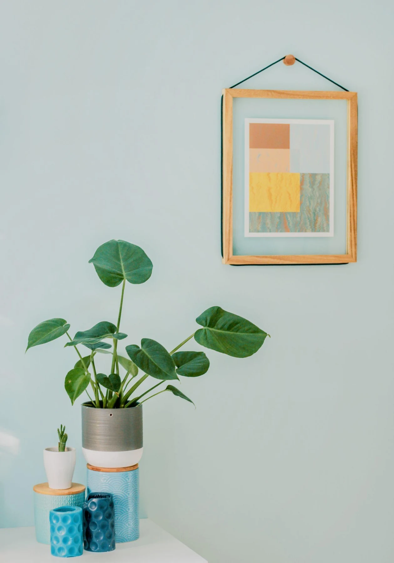 A small square geometric artwork hangs above a compact table and plant.